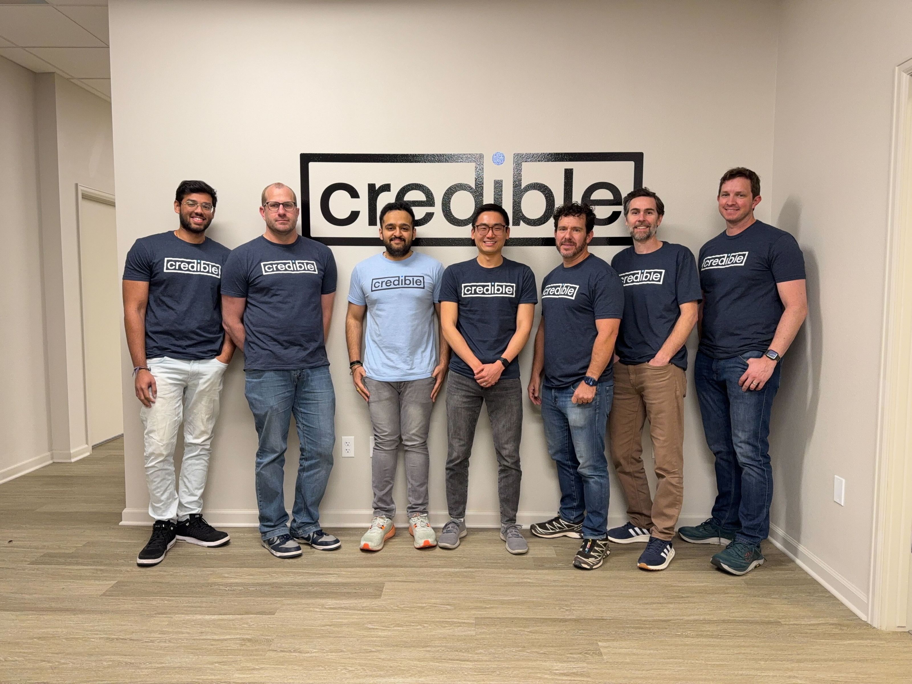 The Credible team standing together in front of the Credible logo